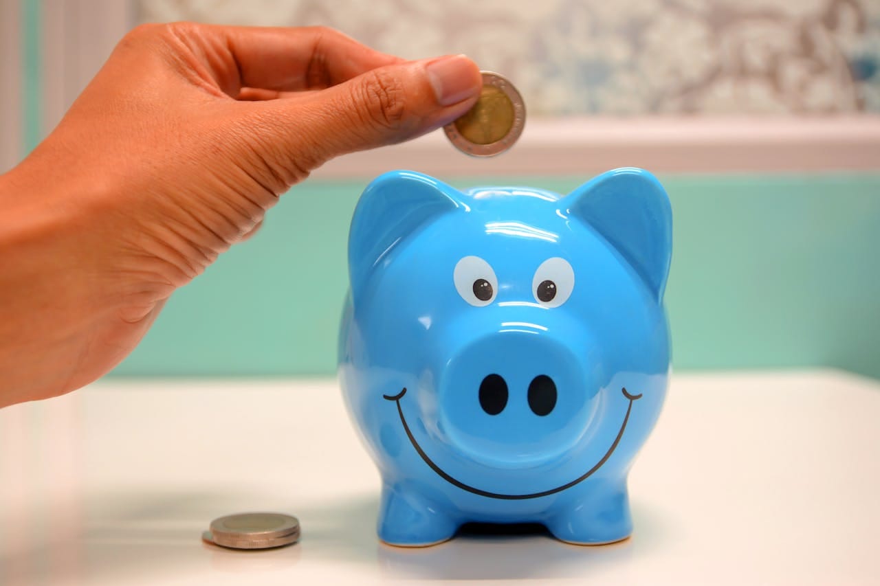 about-us-02 Hand inserting a coin into a blue piggy bank for savings and money management.